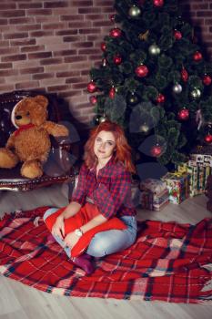 Christmas Gift. New year celebration. Beautiful holdiay decorated room with Christmas tree with presents under it. New Year and Christmas concepts. Beautiful girl sitting near New Year tree.