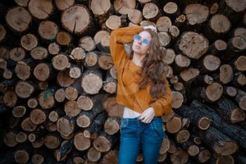 beautiful amazing gorgeous redhair girl spins in yellow sweater, jeans and glasses on the background of firewood. Autumn mood