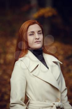 Portrait of a beautiful, dreamy and sad girl with red hair in white coat autumn.
