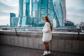 Smiling beautiful woman in a light coat against the backdrop of a skyscrapers business center of a big city. Moscow City