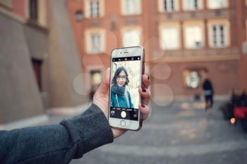 Back close up view of female person holding cellphone with and make photo with street on background. Woman's hands with mobile phone devise, finger touching display