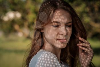 Portrait of a charming young woman outdoor. Light and shadow. interesting portrait of young girl's face covered with unusual shadow