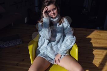 Model with perfect sensual figure pose in home interior. Sexy lady in classic room with sunny light in a gray sweater. The concept and idea of a happy awakening, good morning and comfort at home.