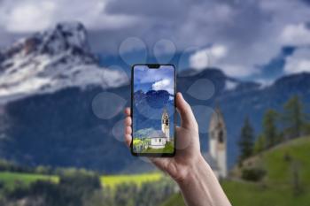 A man makes a photo on a smartphone, beautiful landscape of Tirol. Chapel of St. Mary Magdalene and the bell tower in the valley of Dolomites.The concept of eco-tourism. Dolomites, Italy, South Tyrol
