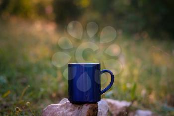 Blue mug of hot tea or coffee with milk, outdoor, Concept adventure active vacations outdoor. Summer camping.