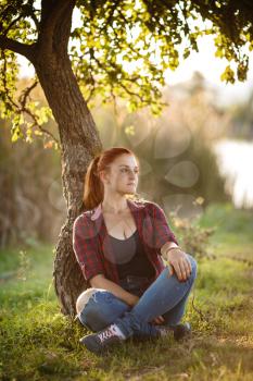 Attractive young woman enjoying her time outside in park with sunset in background. woman dressed in plaid shirt and jeans