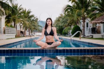 Vacation lifestyle scene of young woman sitting in swimming pool in morning time. Weekend and holiday lifestyle concept, morning meditation by the pool