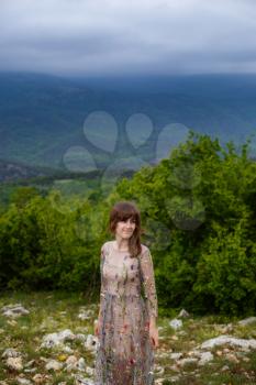 Young happy woman in long dress on the mountainside. Girl on the nature on blue sky background. Fashion photo