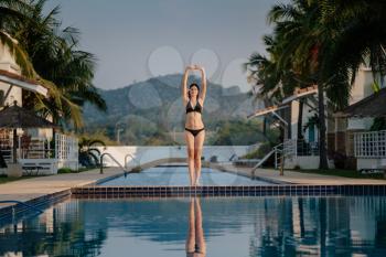 Full length shot of a slim young woman in swimwear at the poolside. Female athlete standing on the edge of the pool and looking away.
