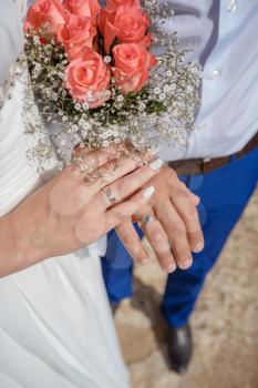 Newlywed couple holding hands and displaying wedding rings, wedding bouquet on altar in church. Hands and rings on wedding bouquet