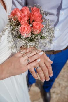 Newlywed couple holding hands and displaying wedding rings, wedding bouquet on altar in church. Hands and rings on wedding bouquet