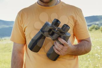 black binoculars in the male hands on the background of an orange t-shirt. The idea and concept of travel, discovery and freedom
