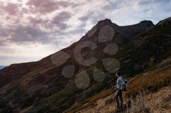 Young male hipster in the mountains in autumn. Discovery Travel Destination Concept. Tourist on the high rocks background. Sport and active life concept.