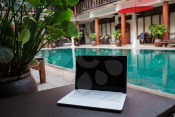 White laptop on the background of the swiming pool. Conceptual workspace. Freelancer, travel and vacation concepts.