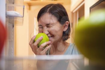 Pretty asian Woman Looking For Food In Refrigerator. healthy food concept. the idea of overeating and delaying stress in quarantine.