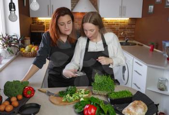 Young girlfriends in the kitchen cooking a vegetarian meal together. Cooking healthy and tasty Shakshuka. woman takes pictures and records video for culinary blog on smartphone