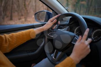Female hands on the steering wheel of a car while driving. Against the background, the forest and road, Close-up