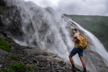 Waterfall Landscape and male Traveler enjoying waterfall view. active vacations into the wild harmony with nature. Image for hiking or climbing. Alibek Waterfall, North Caucasus, Dombai, Russia.