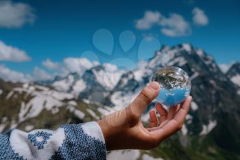 Lens ball glass ball held in a female hand with reflection of Caucasian mountains, Dombai, Russia. the idea and concept of discovery, travel and trekking