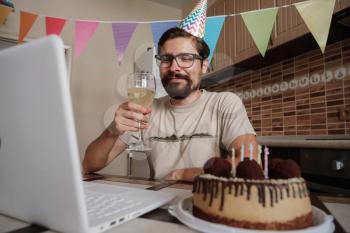 Man celebrating birthday online in quarantine time. Guy celebrating his birthday through video call virtual party with friends. Coronavirus outbreak 2020.
