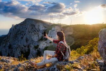 woman hiker enjoy the view at mountain peak cliff, takes pictures on your smartphone or uses apps to communicate.. idea of ecotourism travel. Discovery Travel Destination Concept