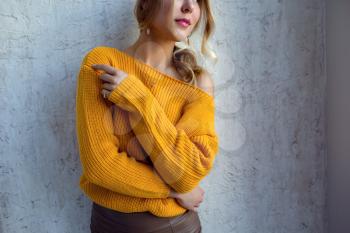 Young woman in a yellow sweater posing against the wall. idea and concept of comfort and tenderness