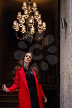 Beautiful young woman in a red coat goes outside from an old house in Istanbul.