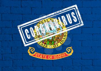 Flag of the State of Idaho painted on grungy brick wall background. with stamp CORONAVIRUS, idea and concept of healthcare, epidemic and disease in USA
