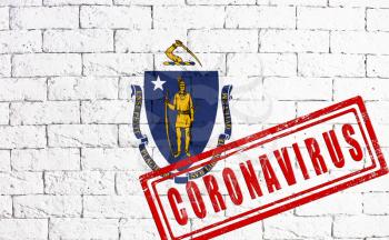 Flag of the State of Massachusetts painted on grungy brick wall background. with stamp CORONAVIRUS, idea and concept of healthcare, epidemic and disease in USA