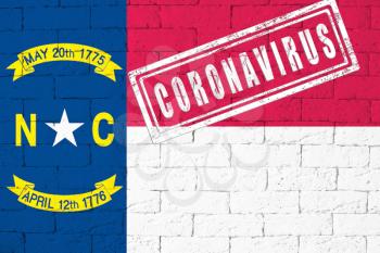 Flag of the State of North Carolina painted on grungy brick wall background. with stamp CORONAVIRUS, idea and concept of healthcare, epidemic and disease in USA
