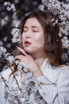 young asian woman in a flowering garden. romantic image of stylish casual woman , trendy silk blouse. positive mood. Cheery Blossom full bloom in Japan.