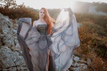 beautiful furious scandinavian warrior ginger woman in grey dress with metal chain mail. Woman is a Viking. Fantasy. Book Cover. beautifully flying dress