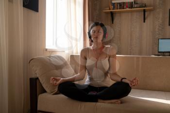 Young woman isolating at home and relaxing: stay at home social media campaign for coronavirus prevention. meditation with smartphone, meditation and relaxation app