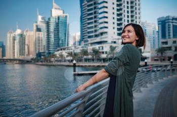 Happy young female traveler in the big city of Dubai, famous place Dubai marina. Luxury and comfortable tourism season in United Arab Emirates.