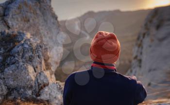 A young man standing on top cliff in spring mountains at sunset and enjoying view of nature. Mountain and coastal travel, freedom and active lifestyle