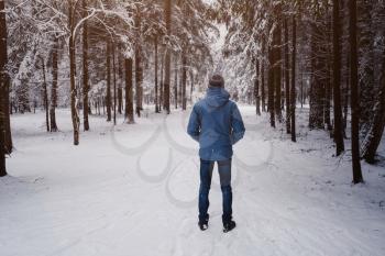 A man breathes deeply in the calm winter forest on a cold day. back view
