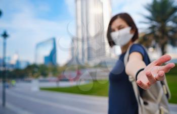 Portrait of beautiful woman wearing a mask for prevent virus walking in Dubai with skyscrapers in the background. Enjoying travel in United Arabian Emirates. Gesture follow me
