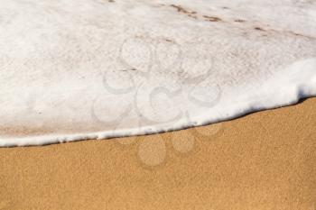 Ocean surf smoothly crossing the warm sand in white foam and bubbles as the waves race onto the beach