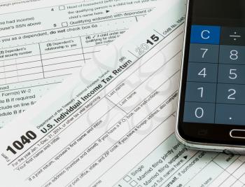 USA tax form 1040 for year 2015 with calculator app on smartphone illustrating completion of tax forms for the IRS