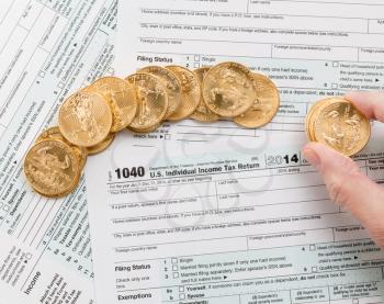 Caucasian hand counting solid gold eagle coins on USA tax form 1040 for year 2014 illustrating payment of taxes to the IRS