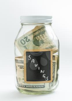 Glass jar on white background with black chalk label or panel and used for savings US dollar bills