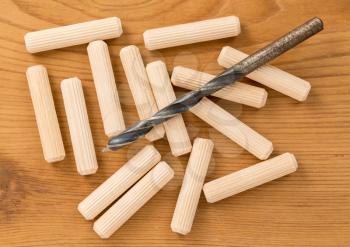 Close shot of set of wooden grooved dowels and drill bit against a wood background