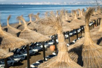 Detail of woven umbrellas above rows of many relaxing beds and loungers on beach