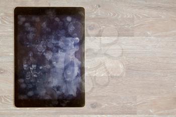 Finger prints and general dust and dirt on screen of touchscreen computing tablet or smartphone on wooden desk