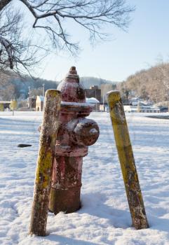 Rusty old fire hydrant in snow field in winter with yellow protective posts