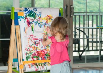 Young two year old girl drawing with pencil on paper mounted on an easel during playtime