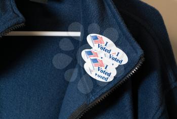 Multiple I Voted stickers with USA flag on blue jacket on hanger illustrating potential voter fraud with illegal votes and need for recount