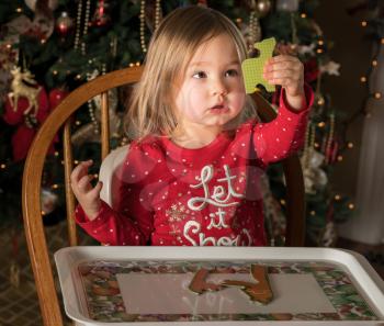 Young female baby girl in high chair making a jigsaw on a plastic tray at Christmas with tree in background