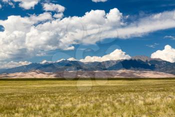 Wide panorama of the dunes at Great Sand Dunes National Park in Colorado with the mountains behind. Unusual to see clouds over the sand