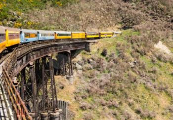 Train and coaches of Taieri Gorge tourist railway run sacross a steel trestle bridge over a ravine on its journey up the valley